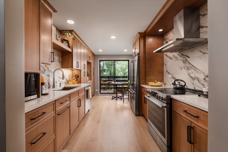 Award-Winning Kitchen Remodel at Valley Lo Towers featuring custom wood cabinetry, white marble-look countertops and backsplash. The space has a sleek, contemporary design with flat-panel cabinets, black linear hardware, and stainless steel appliances.